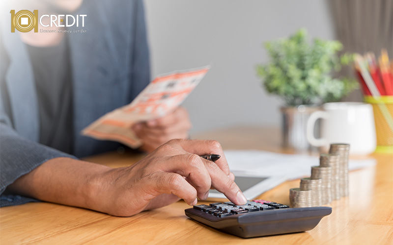 Person using a calculator and reviewing a document at a tidy desk with stacked coins and office items.