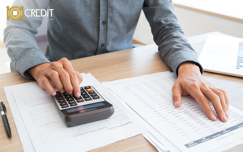 Person using a calculator at a desk with financial papers and a laptop