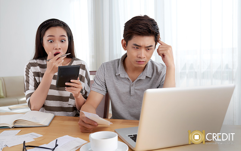 A shocked woman looking at a calculator while a stressed man reviews financial documents