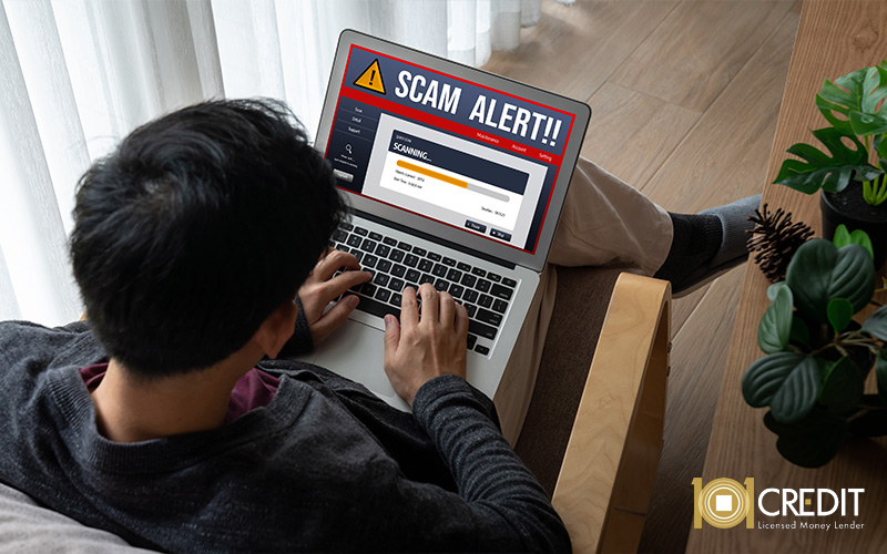 A person using a laptop with a prominent "SCAM ALERT!!" warning on the screen
