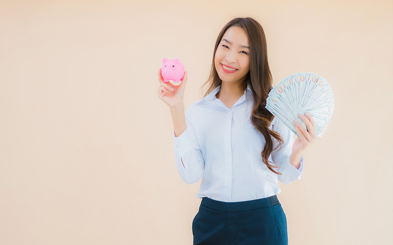 Woman holding piggy bank and cash, managing personal savings.