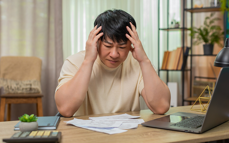 Man holding head in stress surrounded by unpaid bills